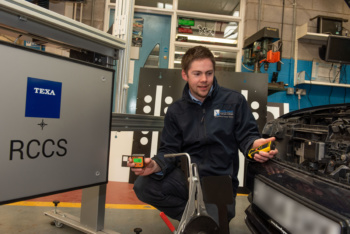 Male in mechanic overalls beside a car engine