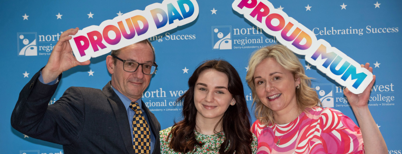 Teenage girl is pictured with her parents at a College Awards Ceremony. The father holds a 'proud dad' sign and the mother holds a 'proud mum' sign