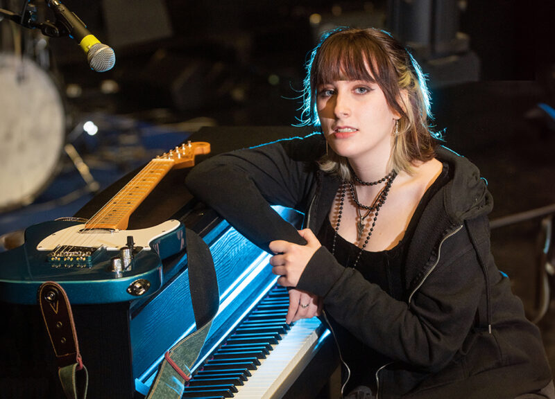 Female Music student Dearbhla Duddy leaning on a piano with a blue guitar placed on top