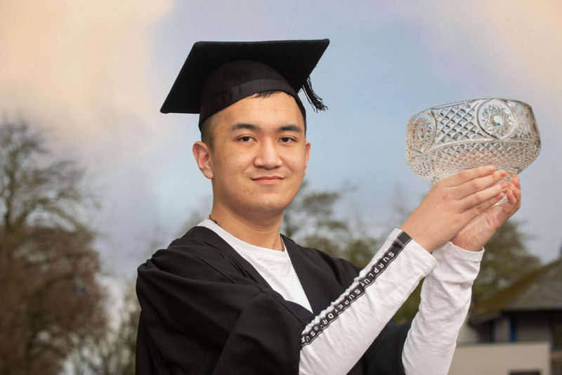 Special award winner, male Chinese graduate Brendan Pang proudly presents his glass trophy.