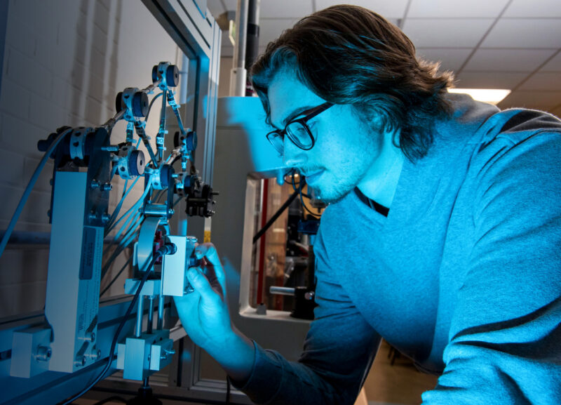 male student Matthew England using engineering equipment with blue lighting