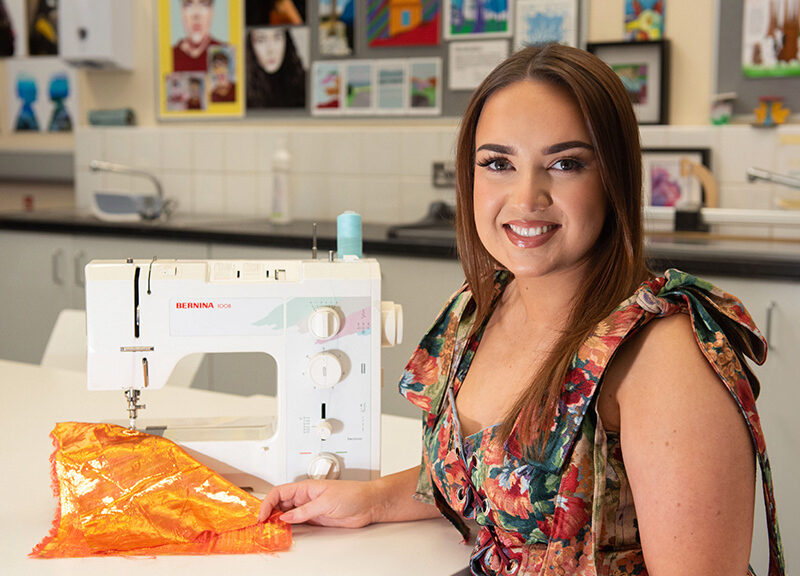 young female student sitting in Art & Design classroom using sewing machine