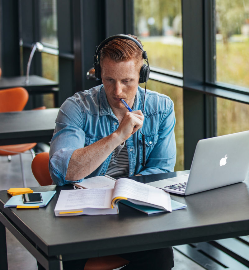 male student studying in library with laptop and headphones