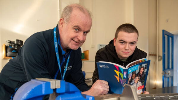 man with blue staff lanyard holds a college prospectus with a young male in workshop