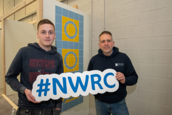 Male student pictured with his lecturer in Tiling workshop, holding 'NWRC' foam board