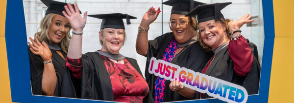 group of female graduates waving and holding photo prop 'I just graduated'