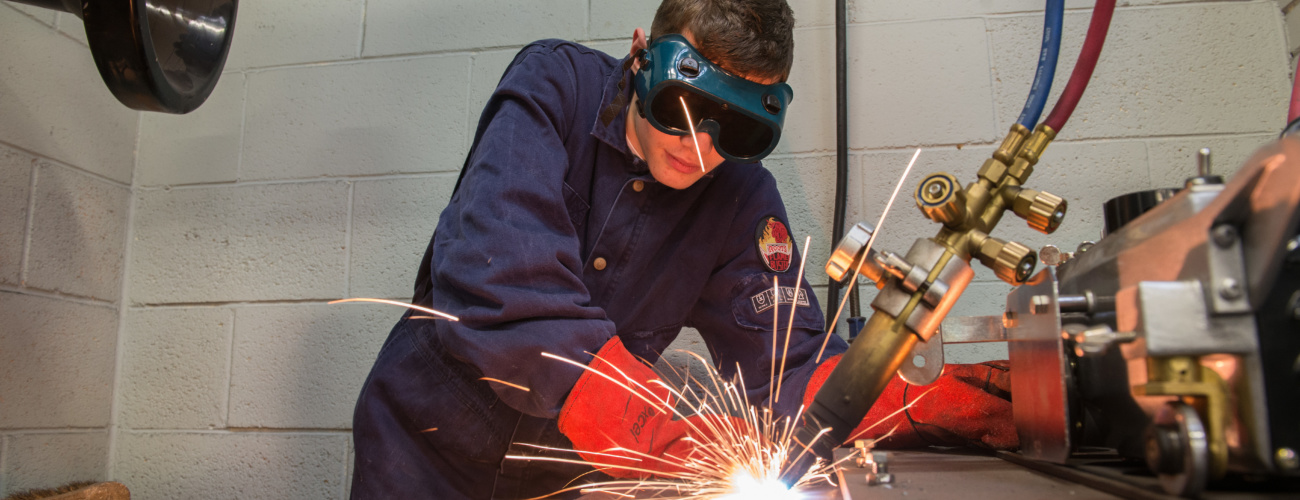 Apprentice in protective clothing using welding equipment