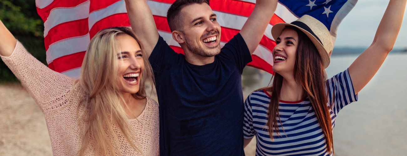Three smiling people walking along a beach, waving a USA flag above their heads