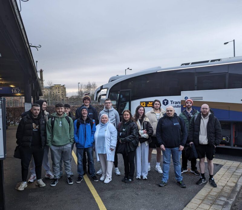12 students and two lecturers holding luggage beside a coach