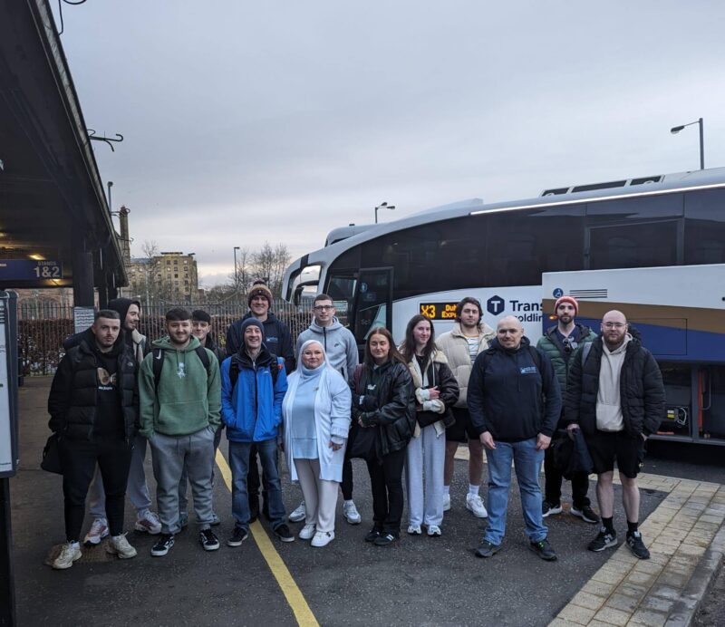 12 students and two lecturers holding luggage beside a coach