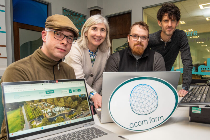 Four people in front of laptops and a sign with Acorn farm written on it