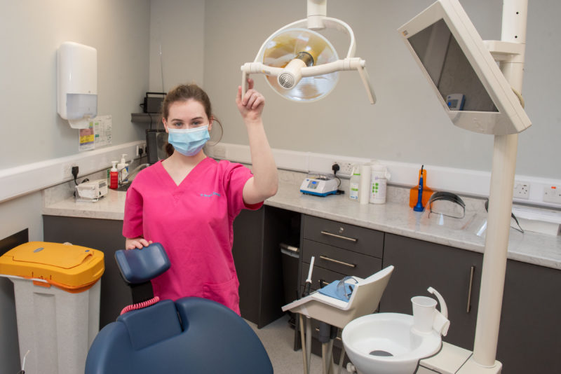 Dental nurse pictured in dental surgery wearing a mask and holding on to the dental chair
