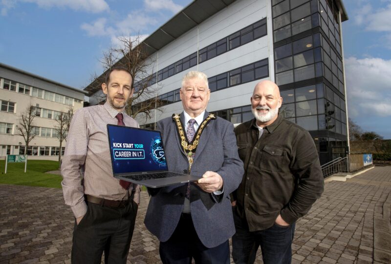 Three men pictured outside a college building holding a laptop