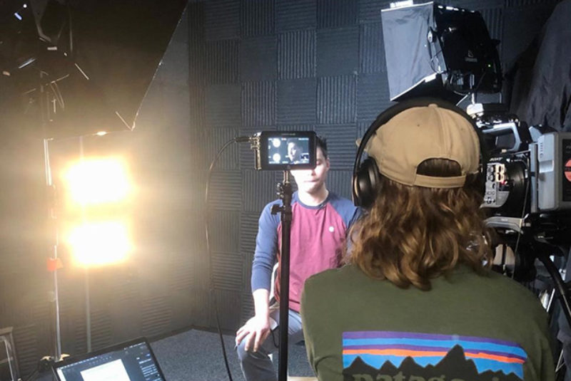 Two male students in film studio with camera and lighting equipment