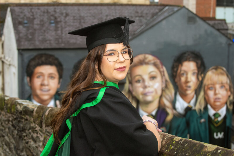 NWRC student in graduation gown and hat picture at the iconic Derry girls mural