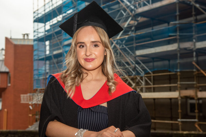 woman pictured in graduation gowns outside a building site