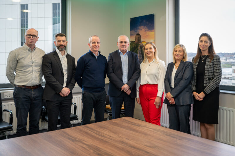 Group of seven people stand in a boardroom