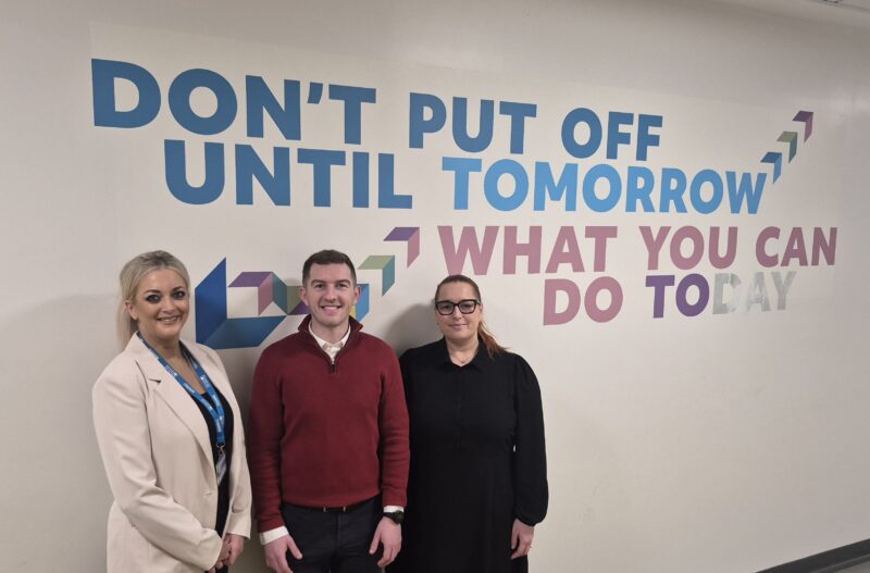 Three people standing beside a wall with an inspiration quote - dont put off until tomorrow what you can do today