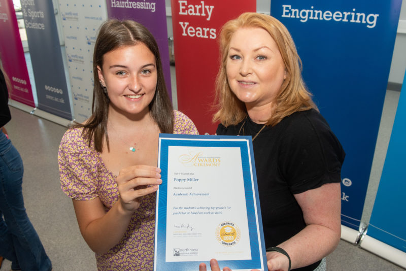 A female lecturer with a female student at an awards ceremony. The two of them are holding a certificate.