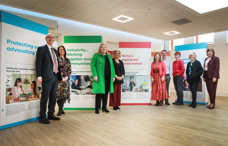 Group of people stand in front of exhibition stands with photos of social workers on them