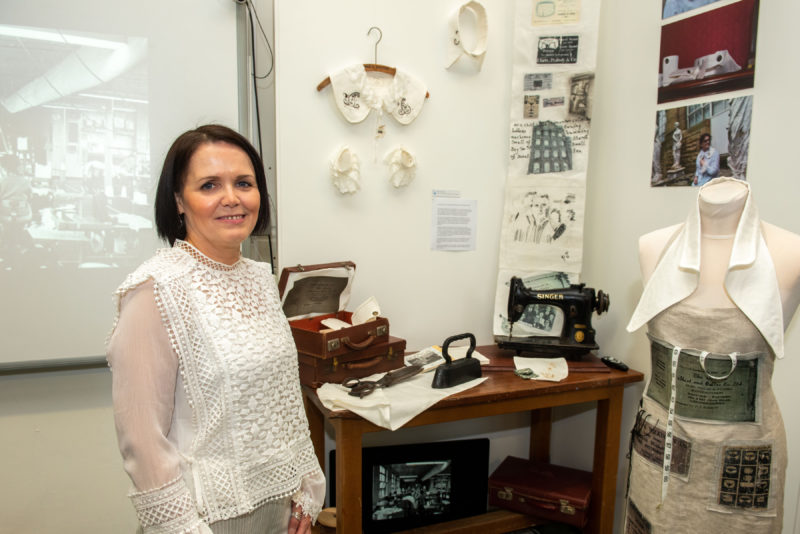 Student in front of her art work which includes a mannequin, sewing machine and prints on the wall.