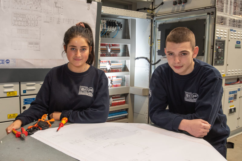 Young male and female electricians in the warehouse with plans in front of them and tools to the side