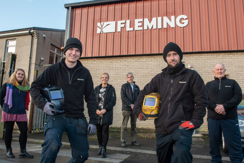 group of people outside a building, with the word Fleming - the two men at the front are holding welding hoods