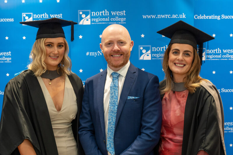 two female graduates smiling with male mc
