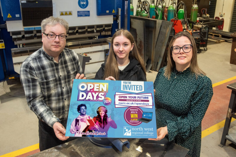 Three people in a welding workshop holding a sign for Open day