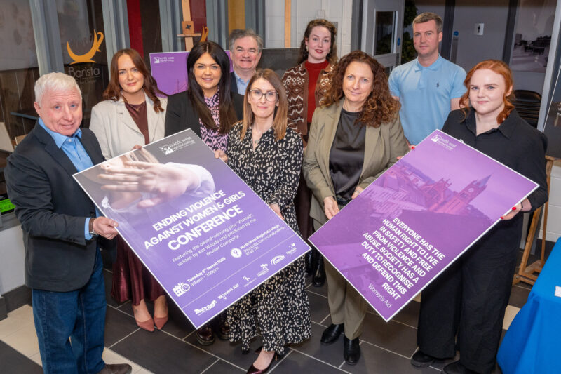 Group of nine people at a conference holding photo props that illustrate the Ending violence against women and girls conference