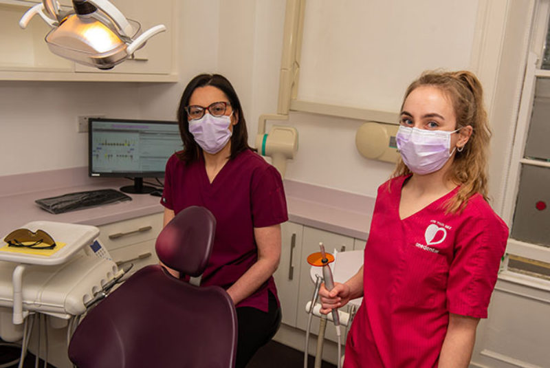 Dentist and dental nurse standing in dental suite holding dental equipment