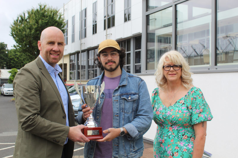 Student is presented with award outside the college building. Also pictured are two other people