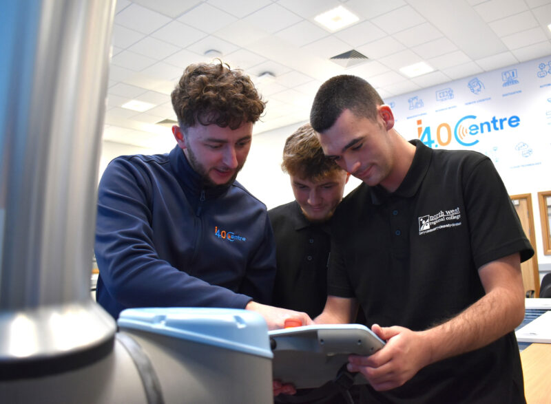 Three men in a factory setting looking at a machine. They are wearing NWRC and 14.0 branded clothing