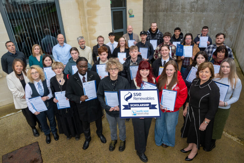 Large group of students hold certificates outside a college building