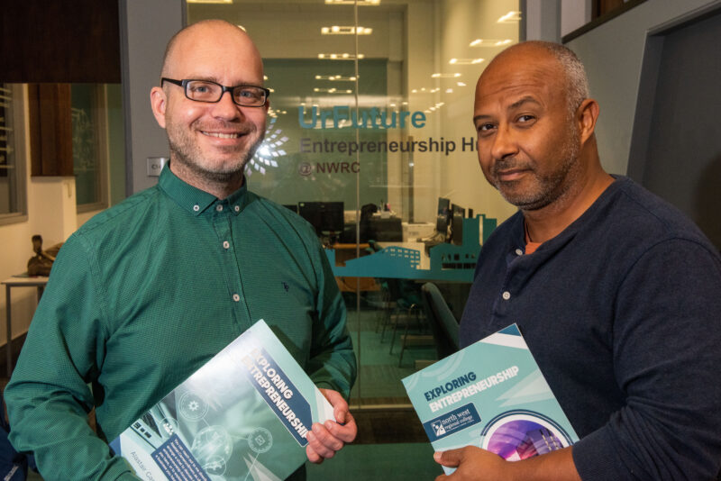 Two men standing outside an office holding an entrepreneurship book