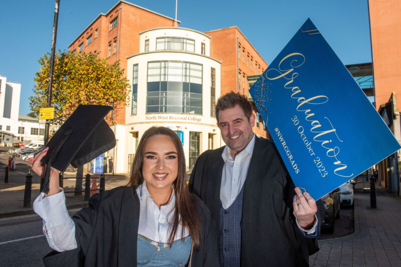 A man and woman wearing graduation gowns and mortar boards outside NWRC's Strand Road campus.
