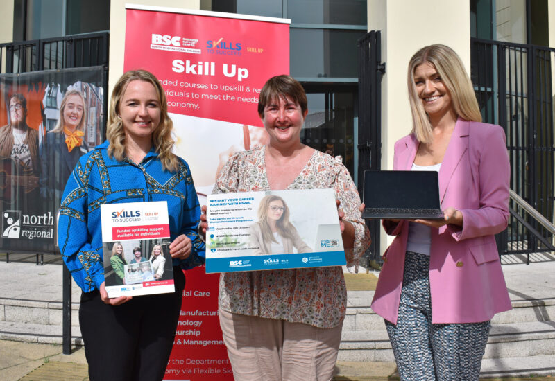 Three women pictured outside a college in the sunshine with a board advertising the women returners programme