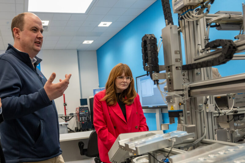 Two people in a robotics classroom. The main is speaking to the woman in the pictures.