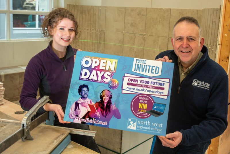 Rebecca and David hold a prop with Open Day on it. They are standing in a tiling workshop
