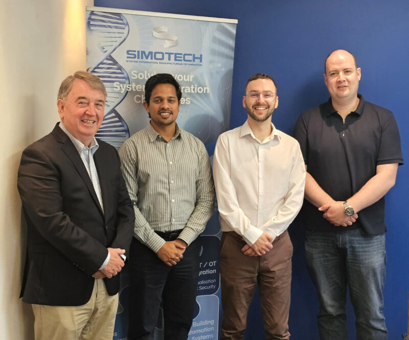 Four people standing in front of branding that states Simotech