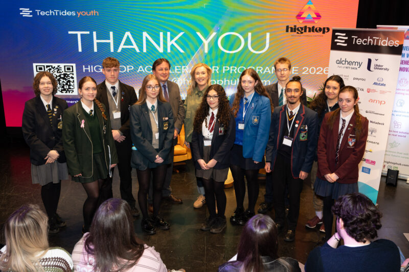 group of people, ten of whom are wearing school uniforms standing in front of branding that states 'Thank You'