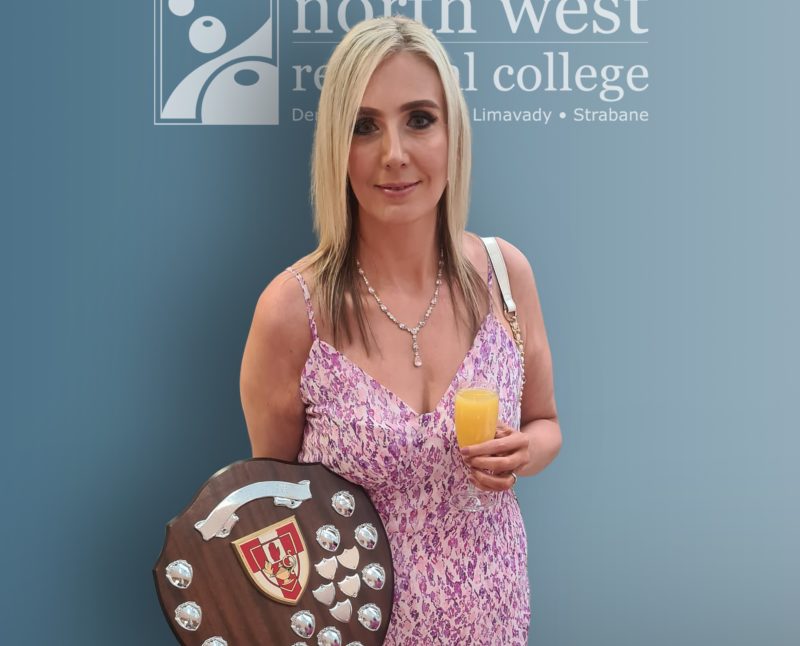 woman in a pink dress holding a shield. The background is NWRC signage