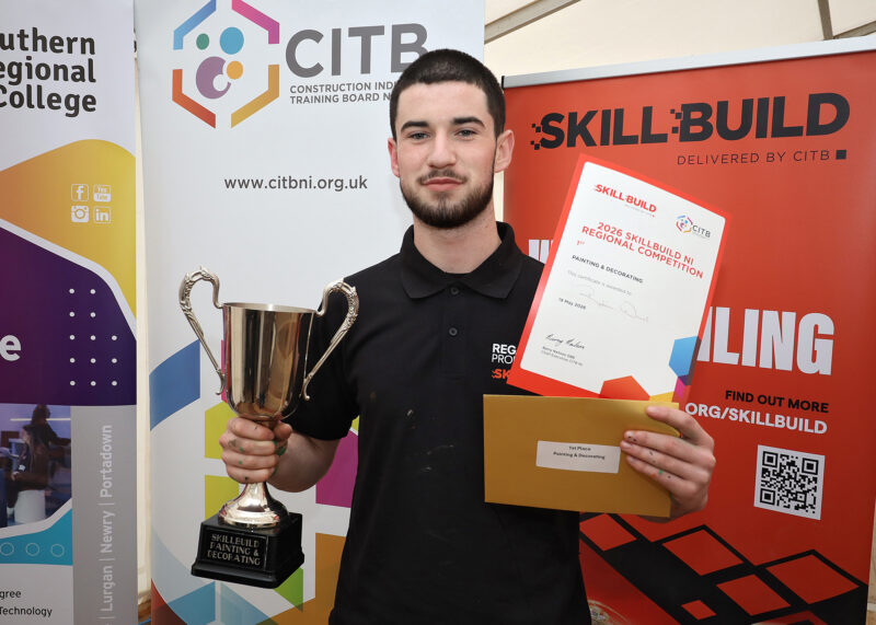 Student apprentice in front of skillbuild and CITB pop ups holding a trophy and certificate