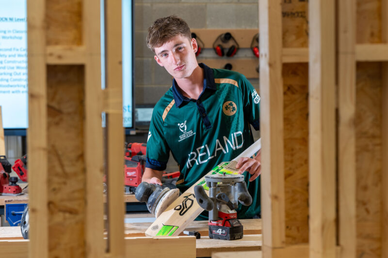 Carpentry student wearing an Ireland top sanding a cricket bat in a workshop