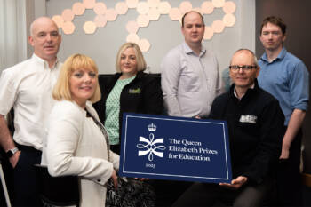 Six people stand together in an office holding a prop that says The Queen Elizabeth Prize for Education