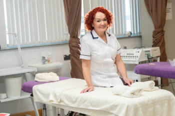 Women in a health tunic leans on a bed in a course area