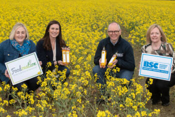 Four people in a field of yellow flowers, One man and three women They are holding signs for Foodovation and Business Support Centre