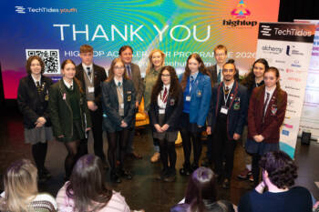 group of people, ten of whom are wearing school uniforms standing in front of branding that states 'Thank You'