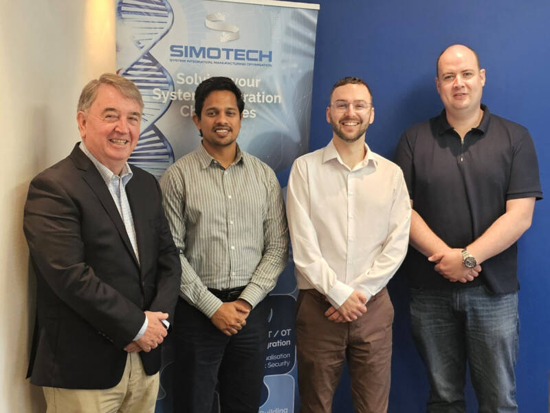 Four people standing in front of branding that states Simotech