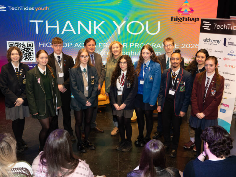 group of people, ten of whom are wearing school uniforms standing in front of branding that states 'Thank You'